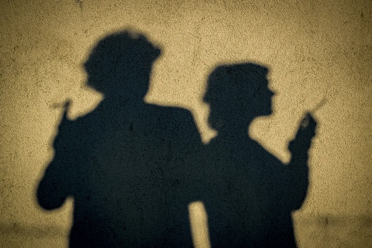 Shadows of two people smoking cast onto a yellow wall